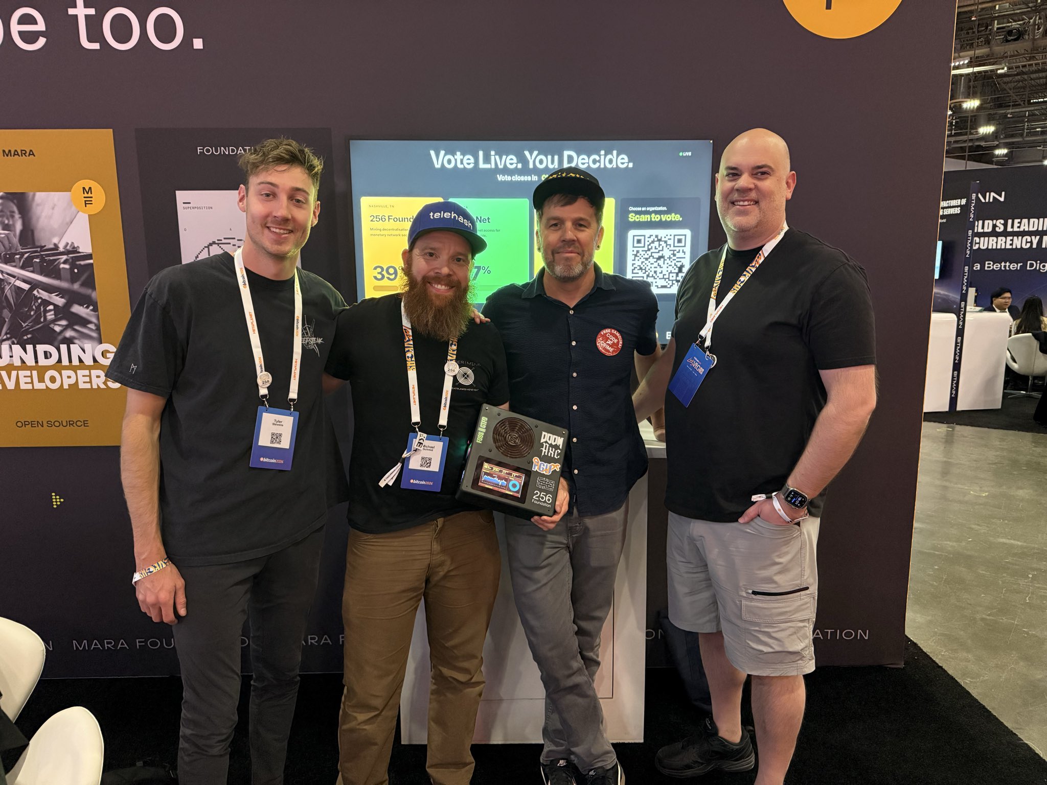 Tyler, Schnitzel, Ryan, and Skot at the MARA Foundation booth as the live vote results show 256 Foundation winning at 39%